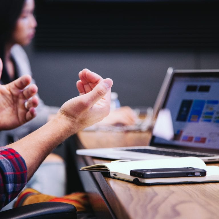 Person gesturing during a meeting with laptop.